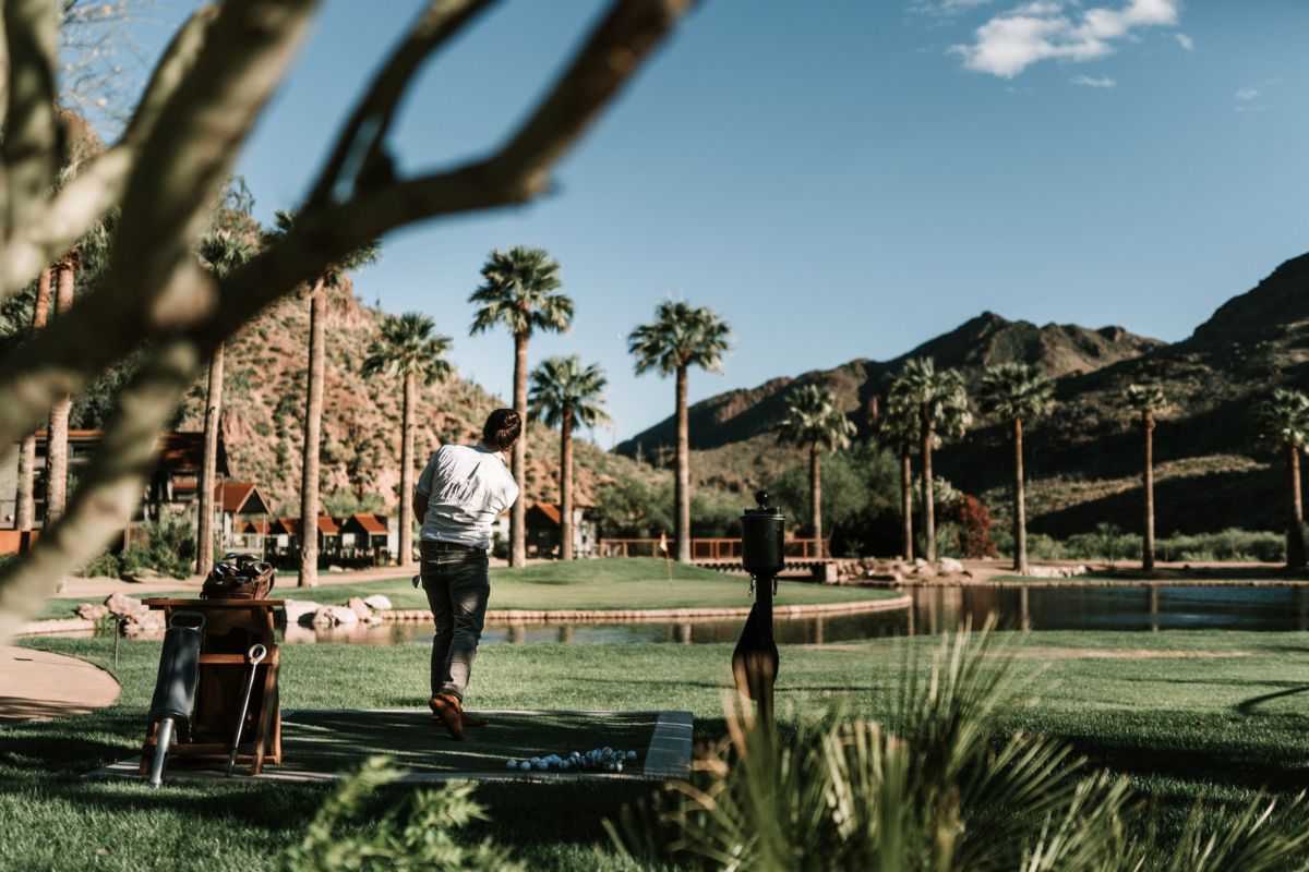 Male golfer hitting the ball on a course with pam trees and mountains